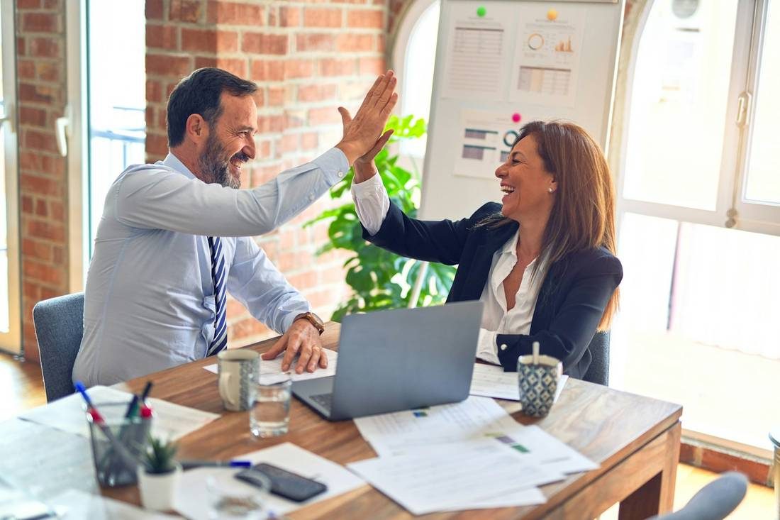 Two colleagues high-five across a meeting table after finishing a piece of work